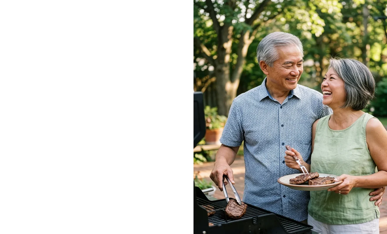 Happy retired couple grilling steaks together in their backyard, smiling at each other.